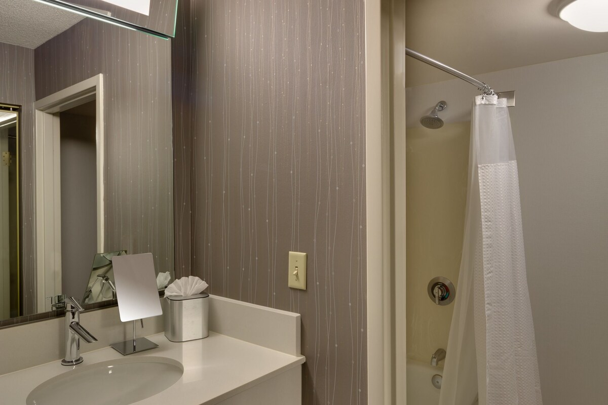Une salle de bain moderne avec un grand miroir, deux lavabos, une douche avec un rideau blanc et un meuble en bois sous le lavabo.