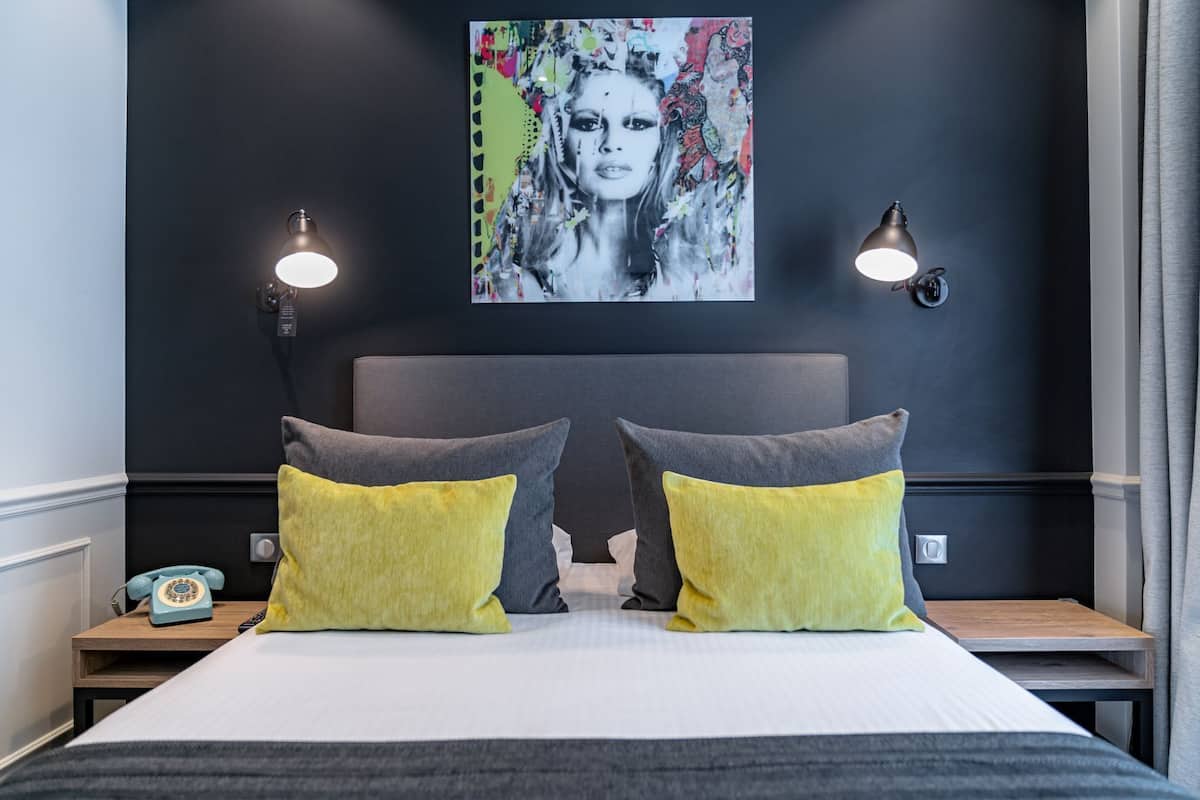 A modern hotel room with a large bed, two bedside lamps, a classic telephone, and a colorful artwork on the wall.