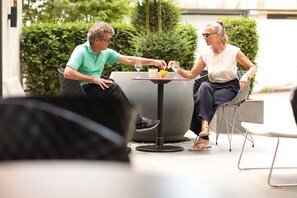 Zwei Personen sitzen an einem Tisch im Freien mit Getränken und Obst.