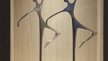 Deux sculptures abstraites en métal, posées sur des piédestaux, sur un fond en bois.