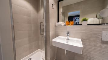 Un baño moderno con ducha envuelta en vidrio, un lavamanos blanco y un espejo grande.