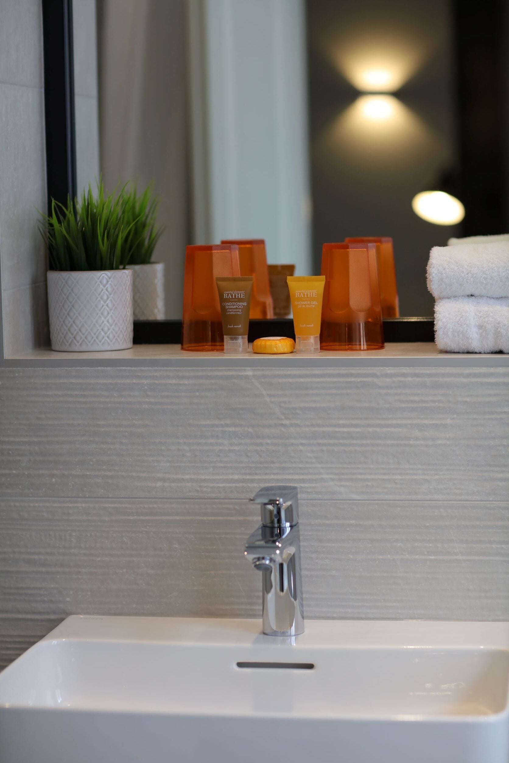 A bathroom with a white sink, a mirror, and toiletries on a shelf.