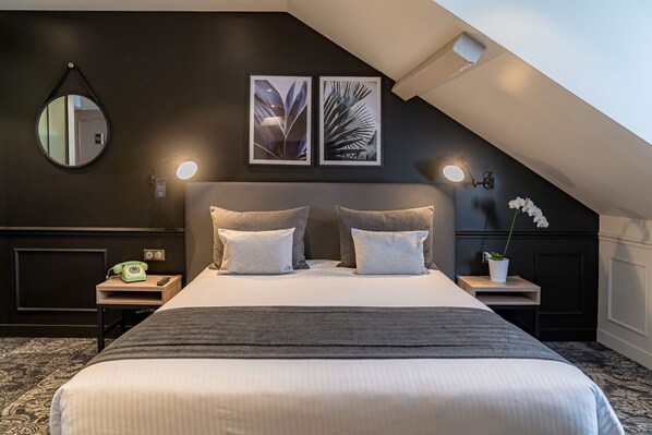 A modern bedroom with a large bed, two bedside tables, a nightstand, a mirror, framed botanical prints, a potted orchid, and a skylight.