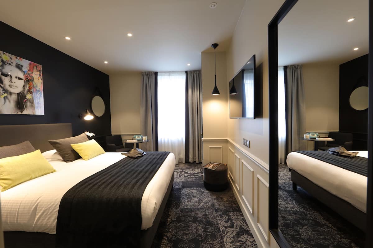 A modern hotel room with a large bed, a bedside table, a mirror, and a painting on the wall.