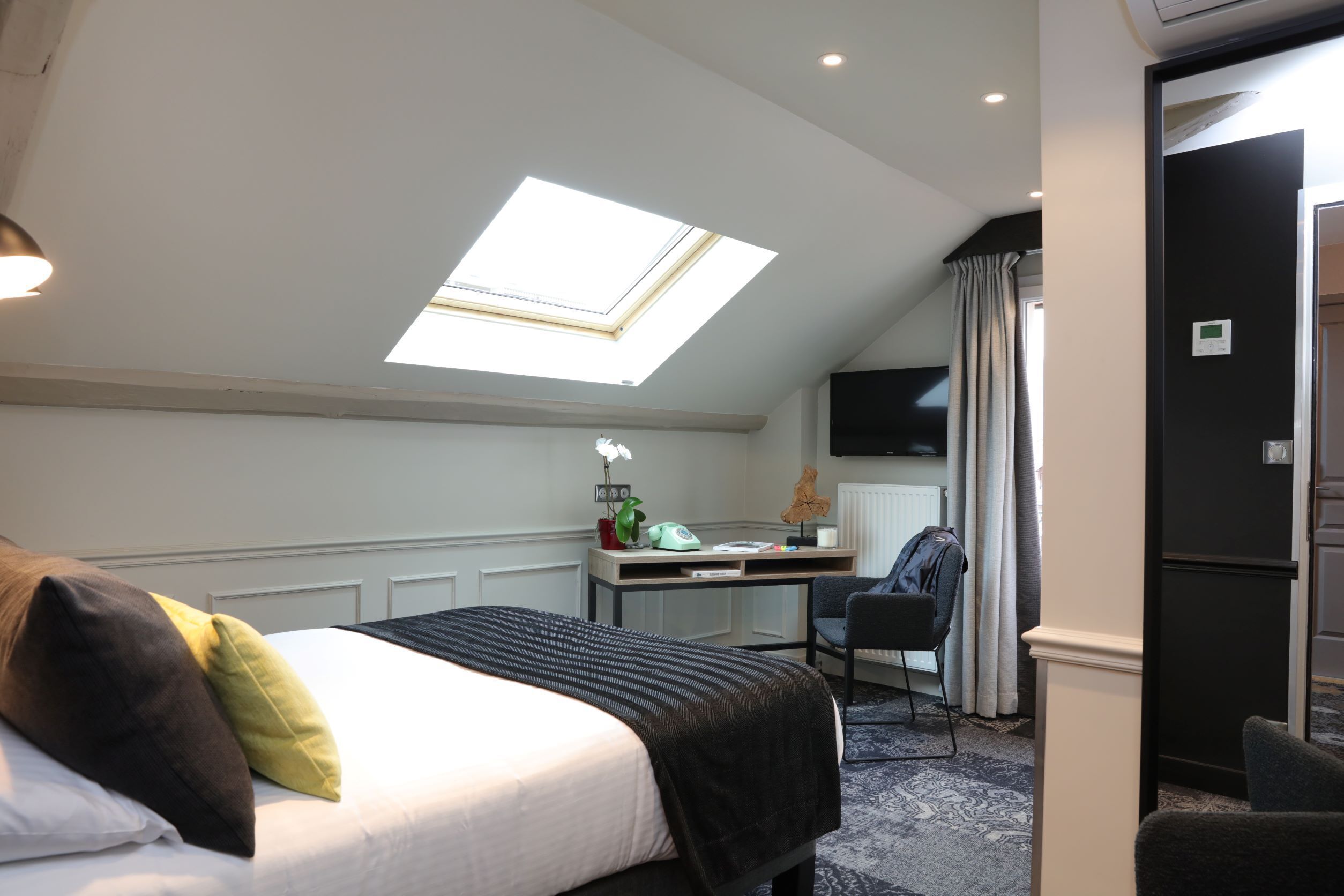 A hotel room with a bed, a desk, a chair, a skylight, and a view of the outside.