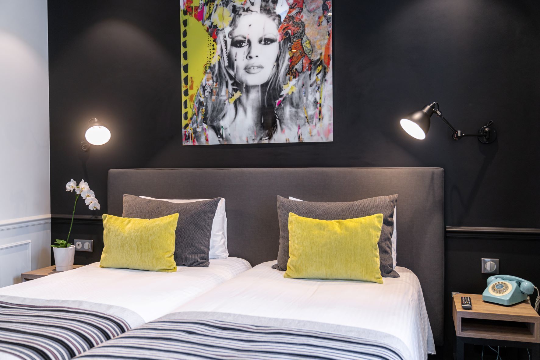 Un dormitorio moderno con una cama grande, dos lámparas de noche, un teléfono antiguo y un cuadro abstracto y llamativo en la pared.