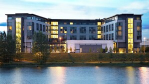 Un edificio moderno de varios pisos con amplios ventanales, techo plano y un cuerpo de agua en primer plano.