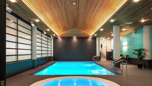 Una piscina interior moderna con hidromasaje, techo de madera y paredes de azulejos.