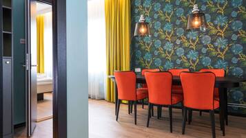 Un comedor moderno con una mesa y sillas, un papel tapiz estampado y vista a una cama a través de una puerta abierta.