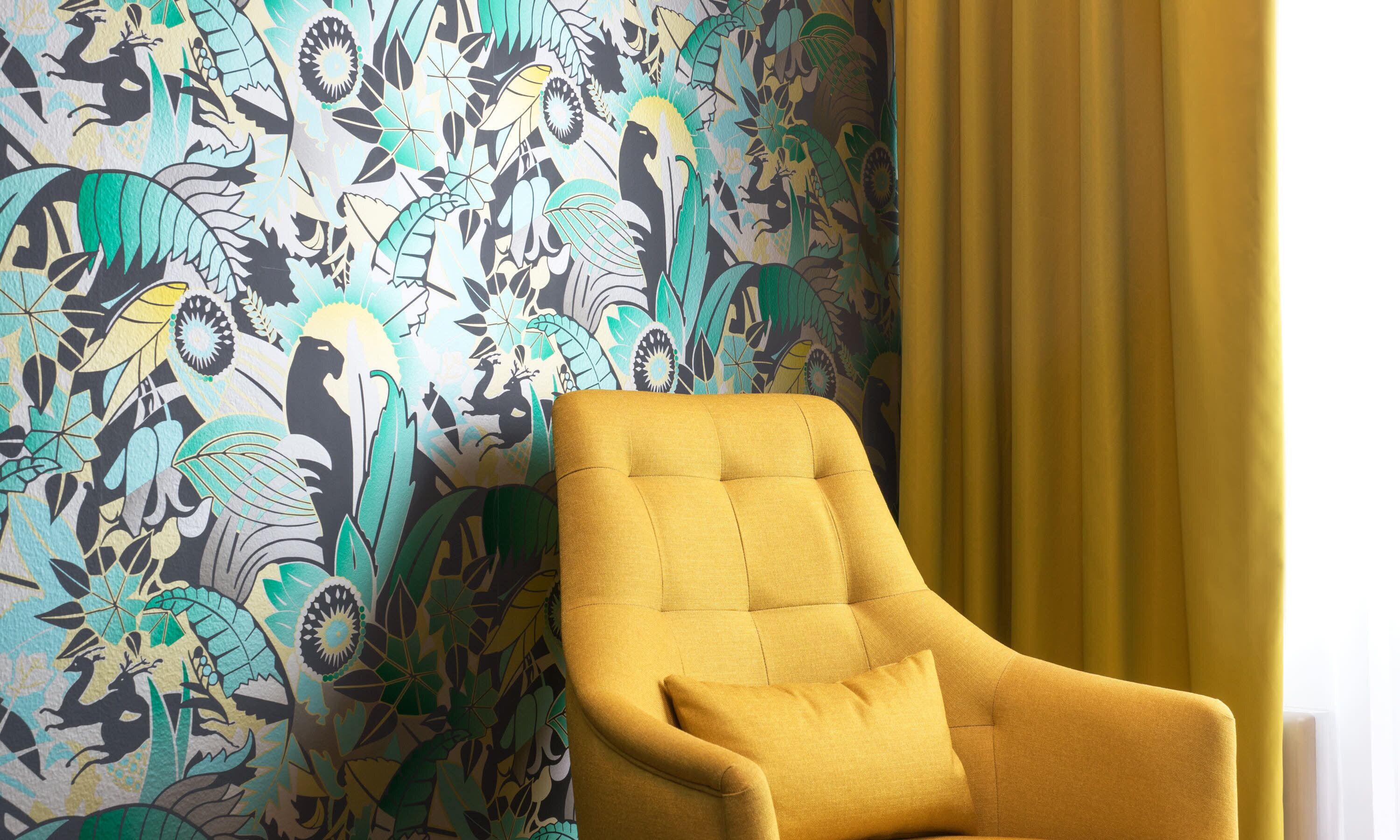 Une pièce avec un papier peint à motifs, un fauteuil jaune et un rideau jaune.