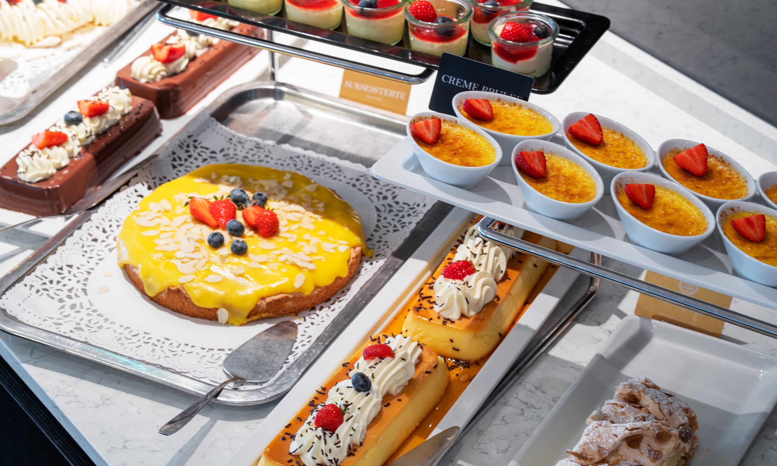A variety of desserts on display, including a large cake with fruit toppings, small bowls of custard, and other sweet treats.