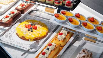 A variety of desserts on display, including a large cake with fruit toppings, small bowls of custard, and other sweet treats.