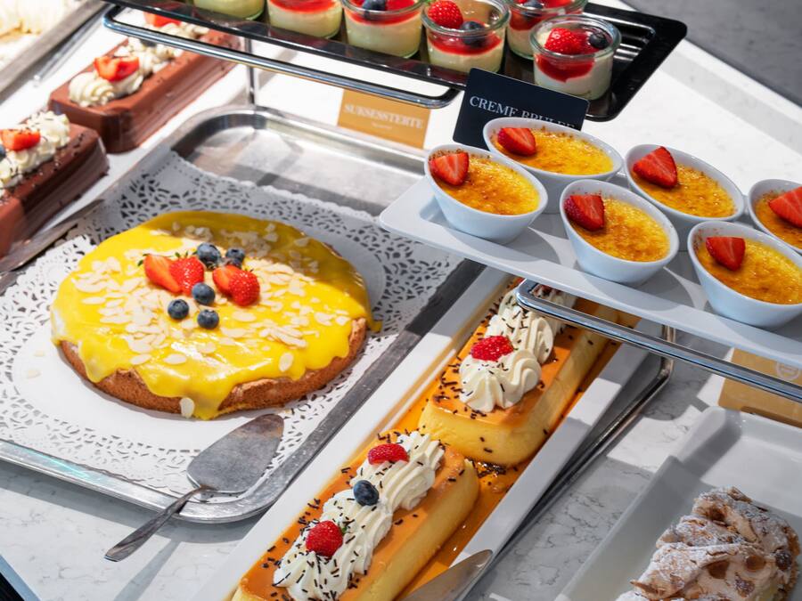 A variety of desserts on display, including a large cake with fruit toppings, small bowls of custard, and other sweet treats.