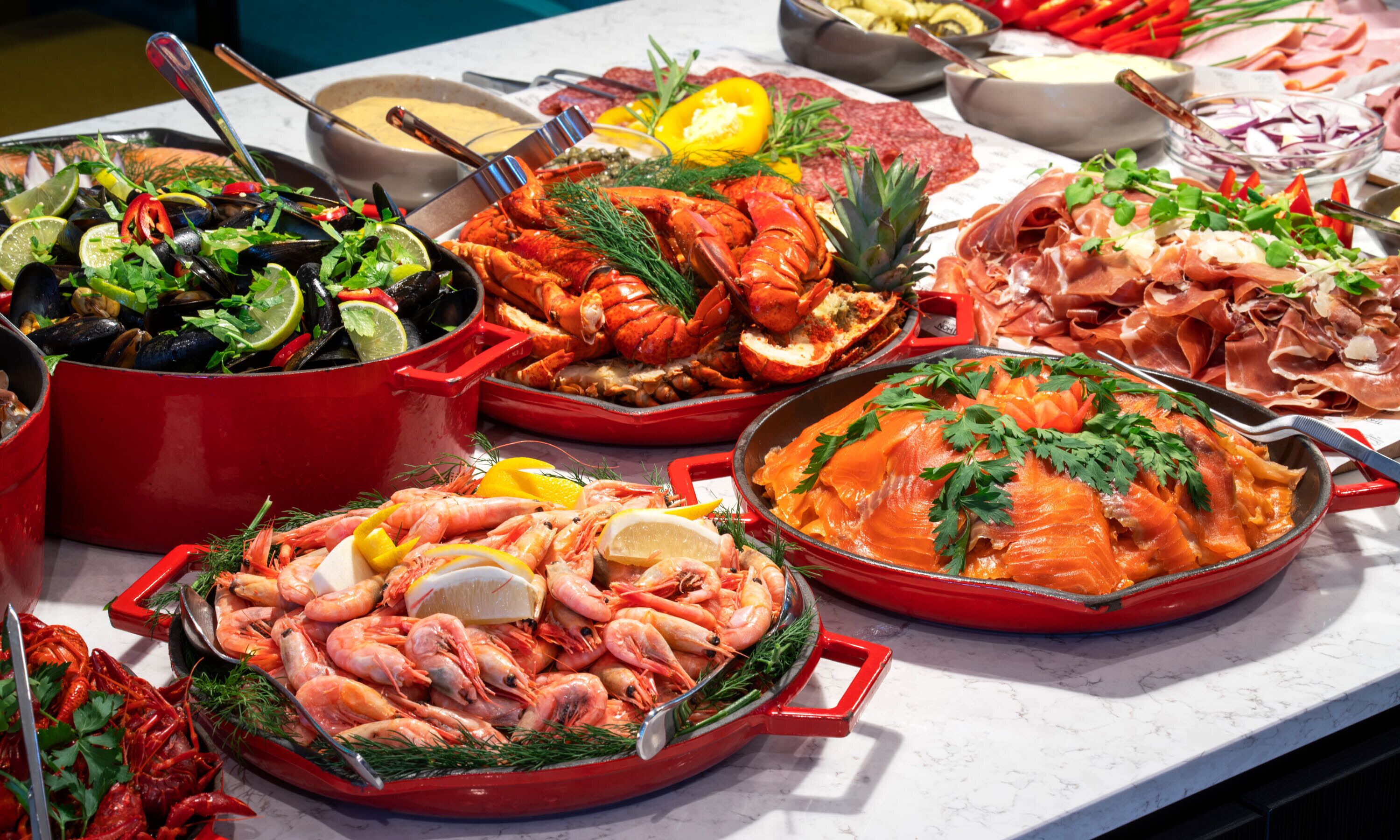 Buffet com diversos pratos de frutos do mar, incluindo camarão, lagosta e salmão, dispostos sobre uma mesa de mármore.