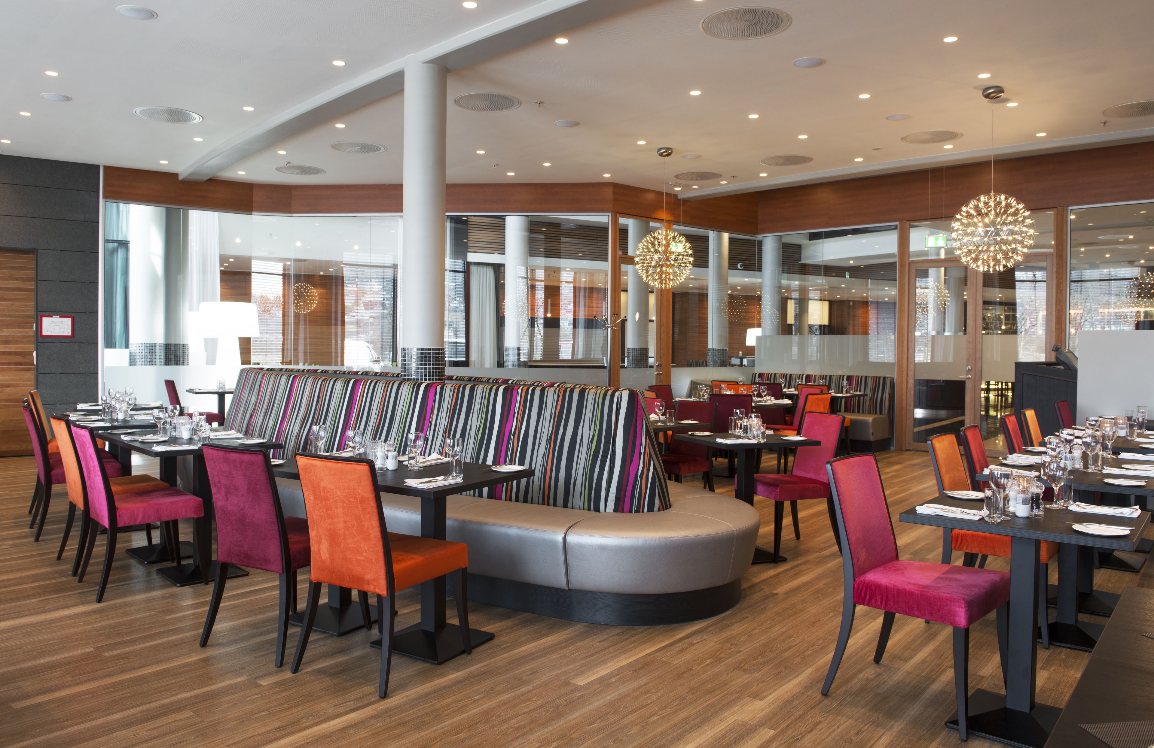Um restaurante moderno com área de estar central, com um banco curvo e mesas com cadeiras ao redor.