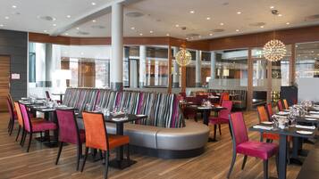 Um restaurante moderno com área de estar central, com um banco curvo e mesas com cadeiras ao redor.