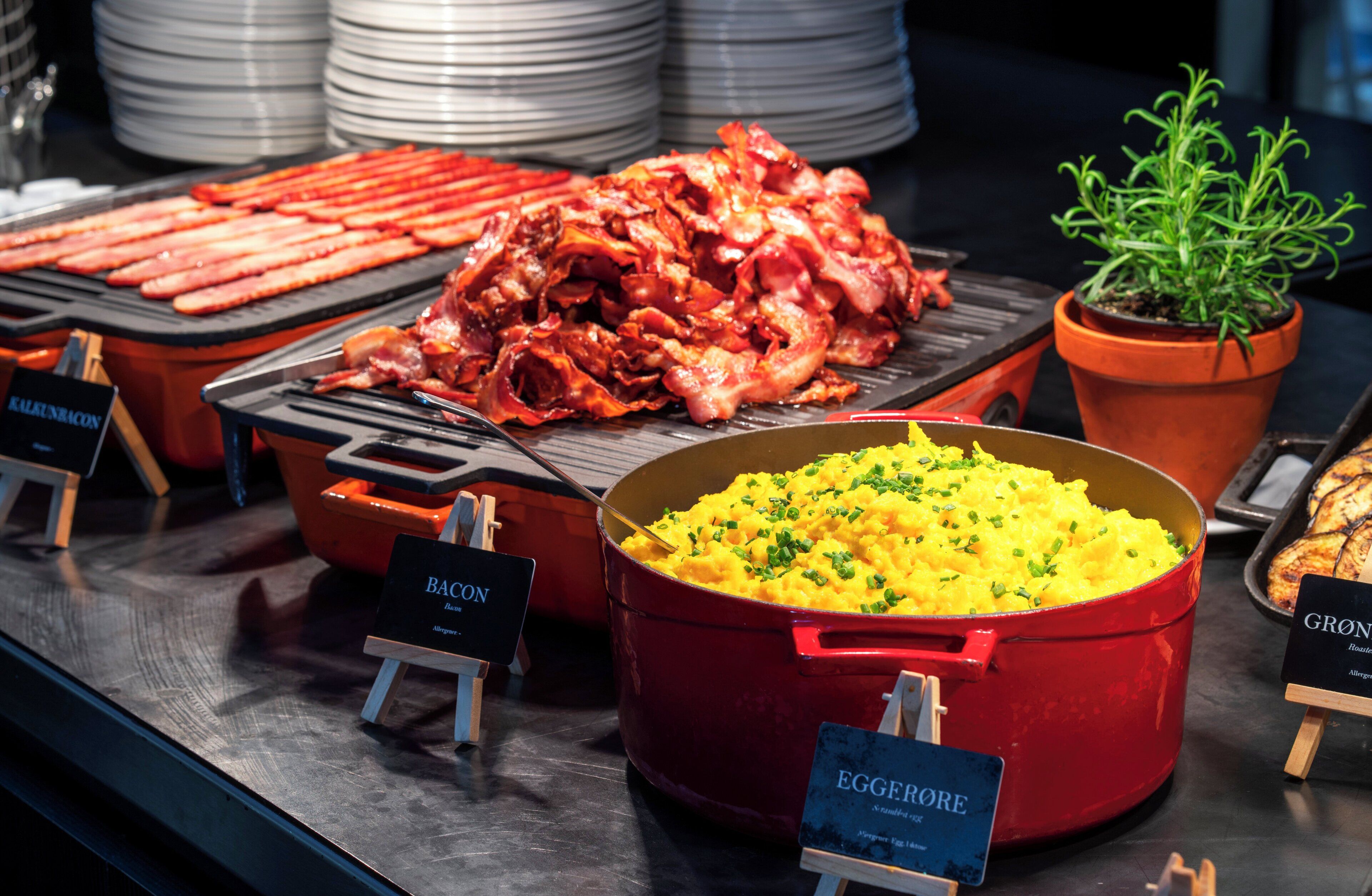 A buffet with various food items including bacon, scrambled eggs, and a red pot of mashed potatoes.