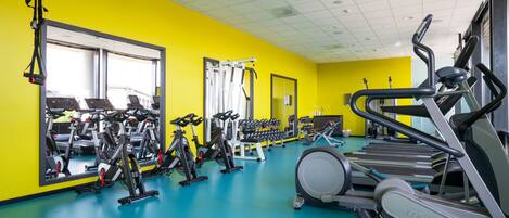 A gym with exercise equipment, mirrors, and a bright yellow wall.