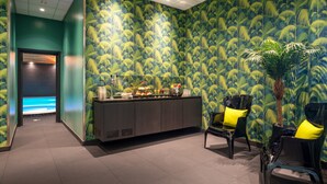 Zona de recepción con papel tapiz de temática tropical, mostrador con diversos artículos y dos sillas con cojines amarillos.