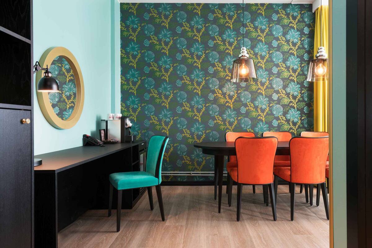 A dining area with a teal and yellow patterned wallpaper, a round mirror, and a black desk with a telephone and a lamp.