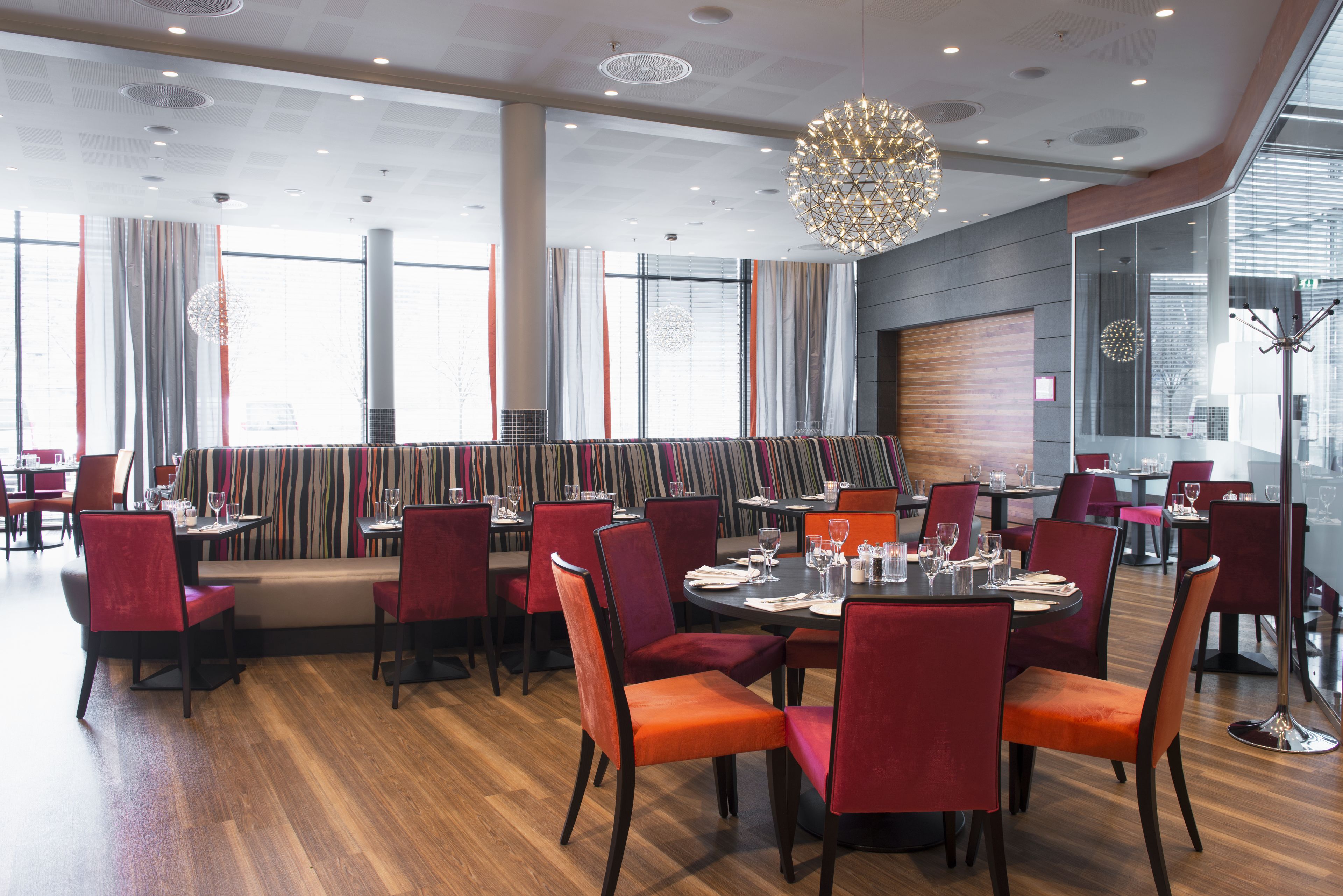 Un restaurante moderno con mesas redondas, sillas rojas y una gran lámpara de araña.