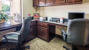 A hotel office with two office chairs, a desk with a laptop, a 'No Smoking' sign, and a window with a view of trees.