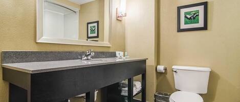 Un baño con lavamanos de superficie oscura, inodoro blanco, espejo grande y un cuadro en la pared.