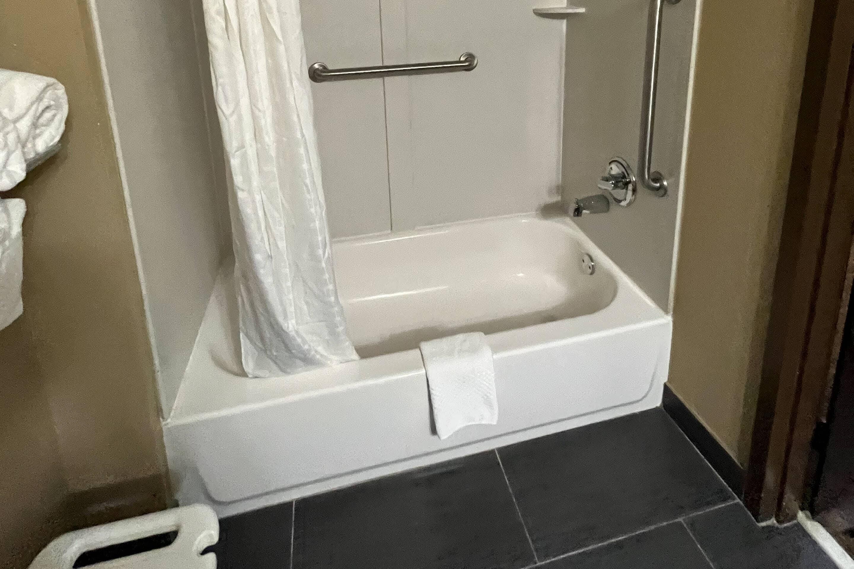 A white bathtub with a towel, a shower curtain, and a grab bar.