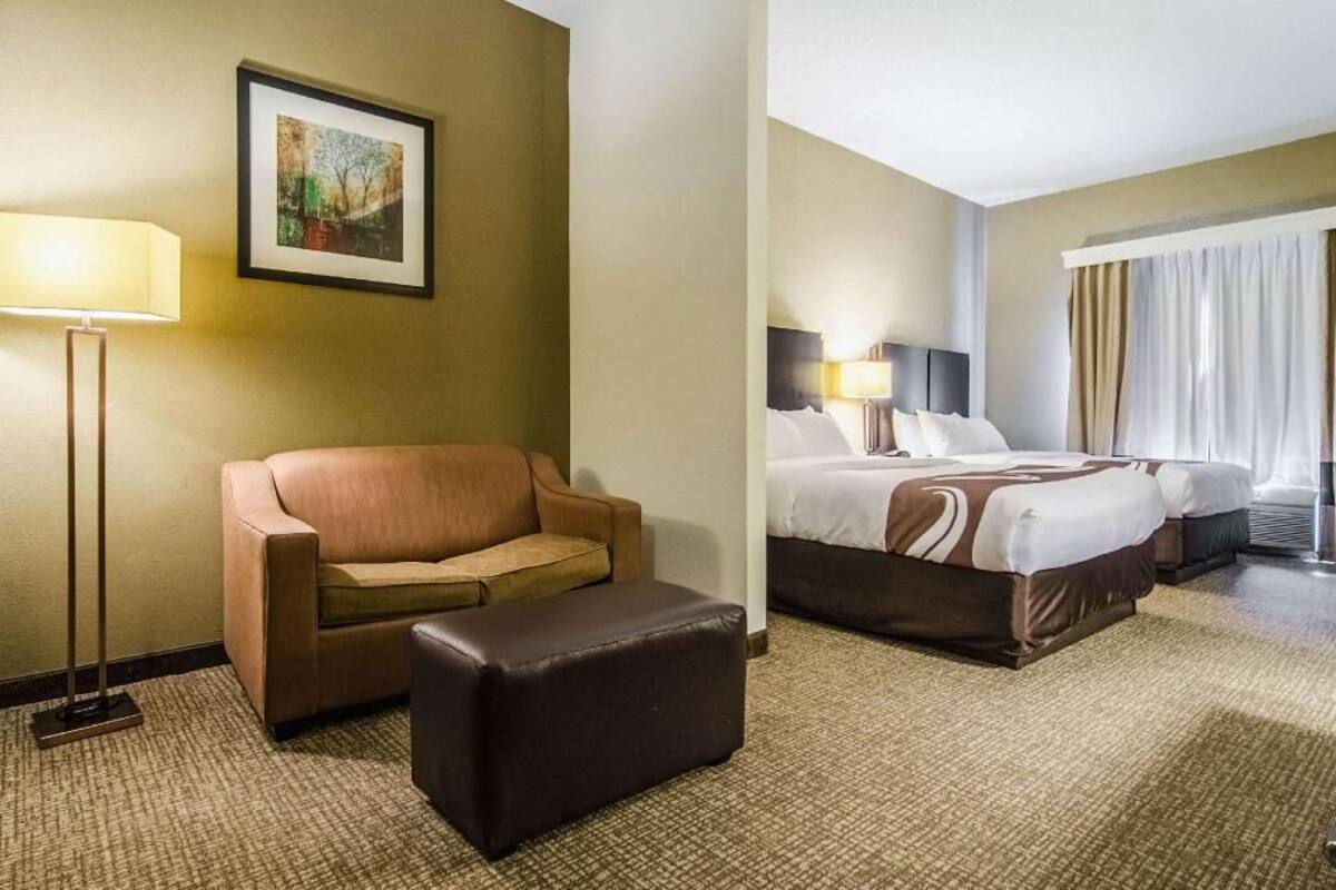 Habitación de hotel con sofá, un pequeño reposapiés, cama con dos almohadas, lámpara y un cuadro en la pared.