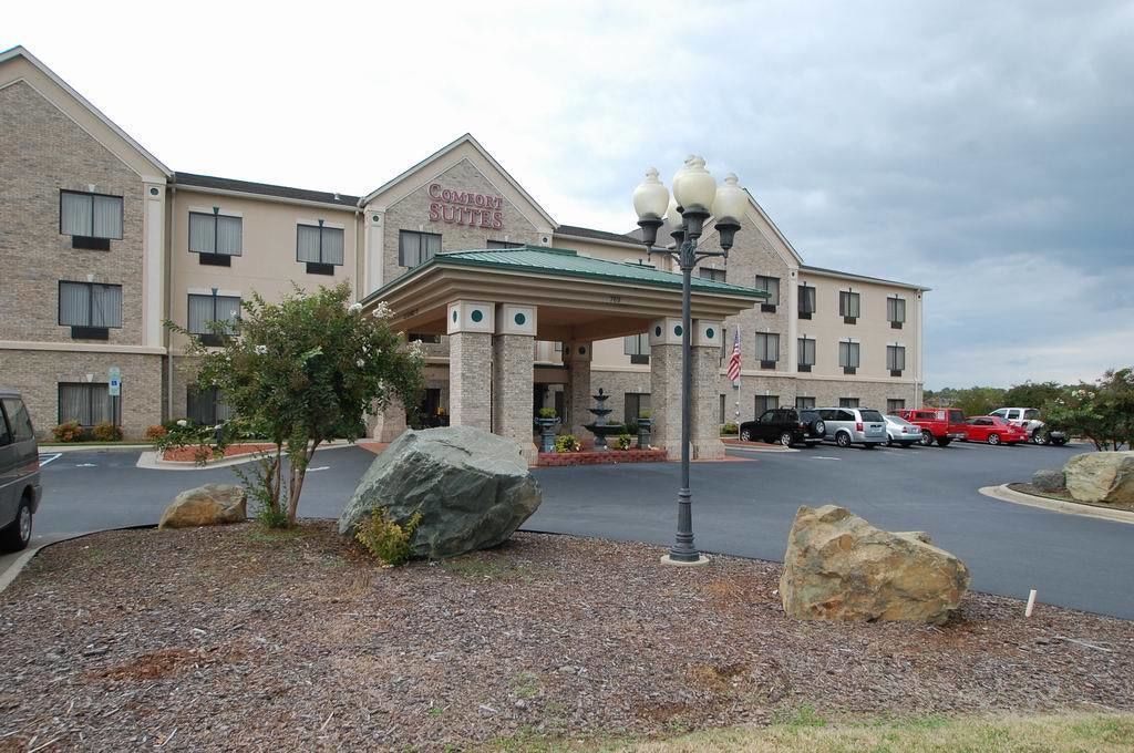 A hotel with a brick facade, a covered entrance, and a parking lot with several cars.