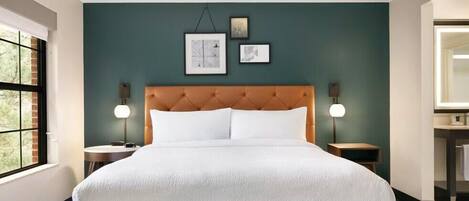A hotel room with a large bed, two bedside tables, a window, and artwork on the wall.