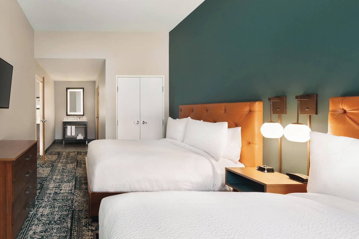 A hotel room with two beds, a large mirror, a wardrobe, and a bedside table with lamps.