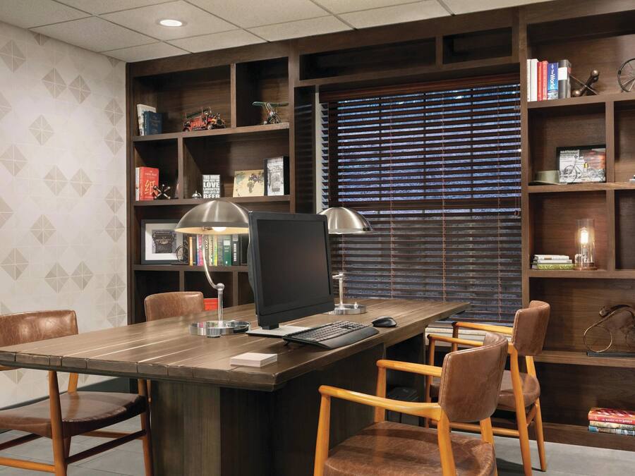 A modern office with a wooden desk, two leather chairs, a computer, and a bookshelf filled with books and decorative items.