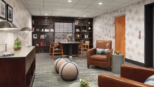 A modern living room with a kitchen area, featuring a leather sofa, a coffee table, and a bookshelf. - Four Points by Sheraton Raleigh Arena (Raleigh)
