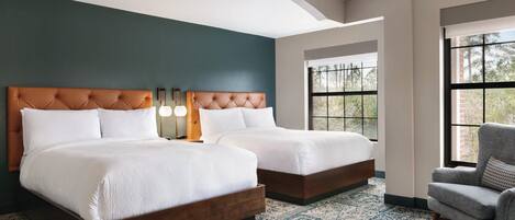 A hotel room with two beds, a patterned rug, a chair, and a large window.