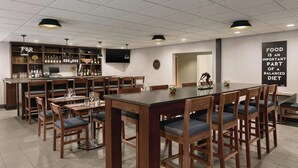 A restaurant with wooden tables and chairs, a bar area with shelves of bottles, and a wall with a food and diet sign. - Four Points by Sheraton Raleigh Arena (Raleigh)