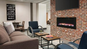 A modern lounge area with a brick wall, a flat-screen TV, a fireplace, and comfortable seating. - Four Points by Sheraton Raleigh Arena (Raleigh)