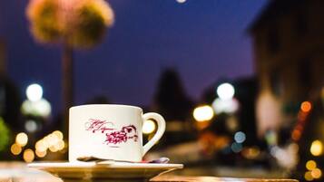 A white mug with a red design on a saucer, placed on a table with a blurred cityscape background.