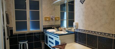 Un baño con bañera, dos lavamanos, tocador con cajones, espejo y ventana.