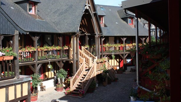 A traditional wooden building with multiple balconies, wooden staircases, and potted plants. - Hotel La Diligence (Honfleur)