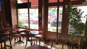 A restaurant interior with wooden tables and chairs, large windows with a view of parked cars outside. - Hotel La Diligence (Honfleur)