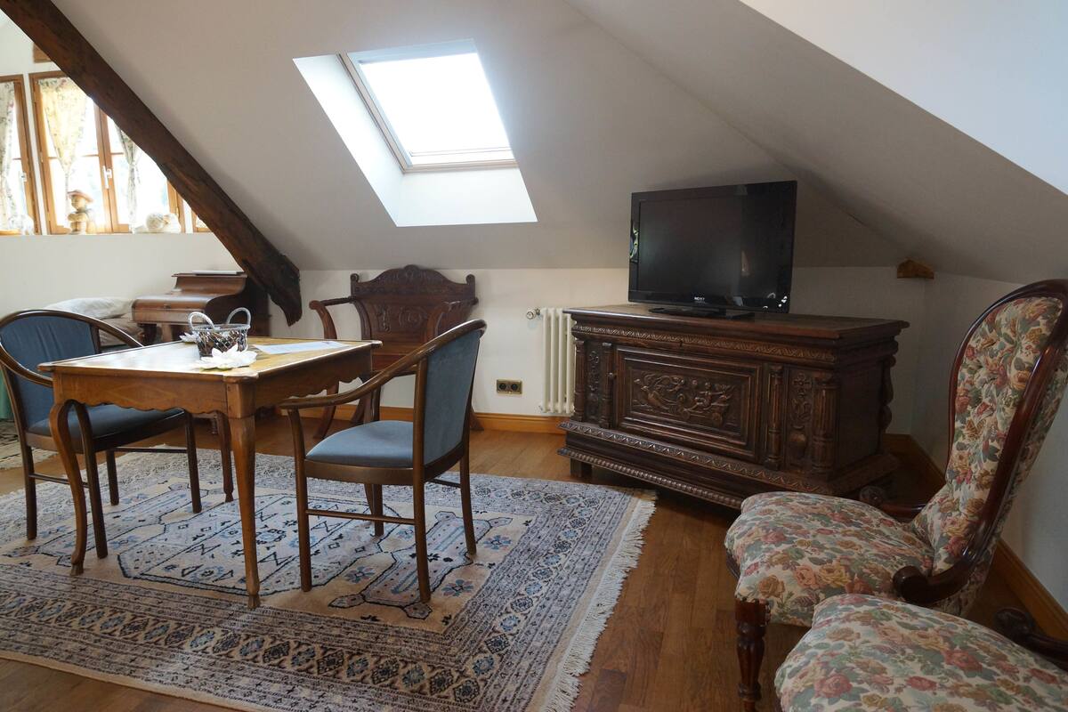 A cozy attic room with a skylight, wooden furniture, and a television.