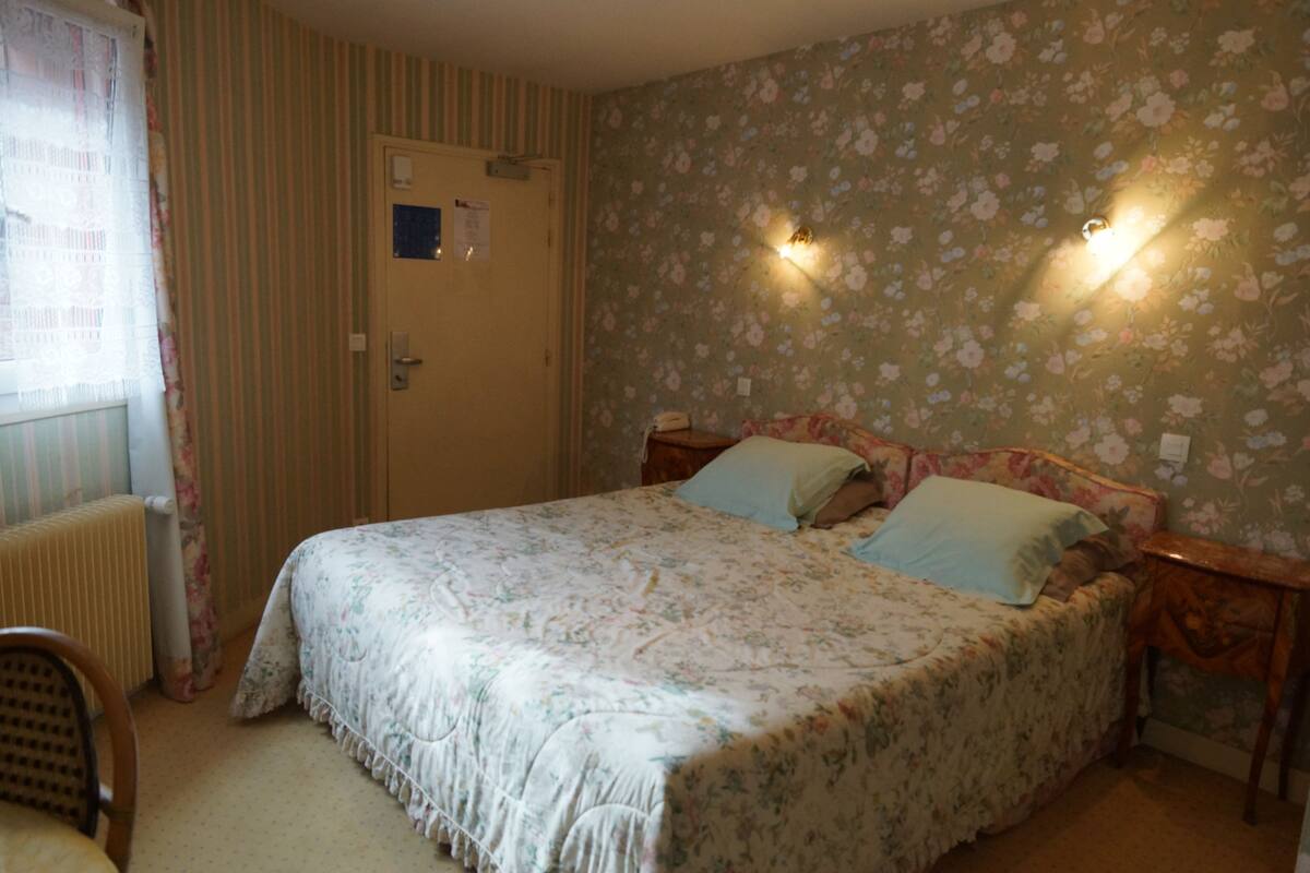A bedroom with a floral-patterned bedspread, a wooden headboard, two bedside tables, and a radiator.