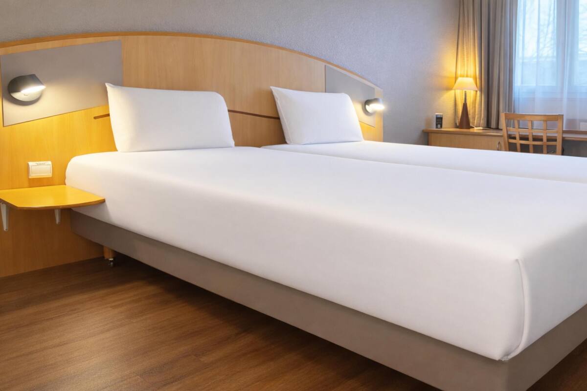 Una cama doble con ropa blanca, un cabecero de madera, mesitas de noche y una lámpara.