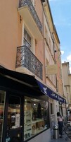 Un hotel boutique con fachada clásica, un balcón con barandilla de metal ornamentada y una tienda con un letrero que dice 'Art et Signature'.