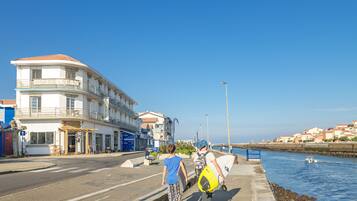 A coastal hotel with a balcony, a street in front, and a body of water.