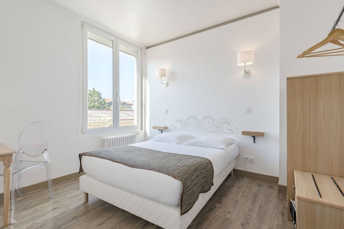 A bedroom with a bed, a chair, a radiator, a wooden wardrobe, and a window.