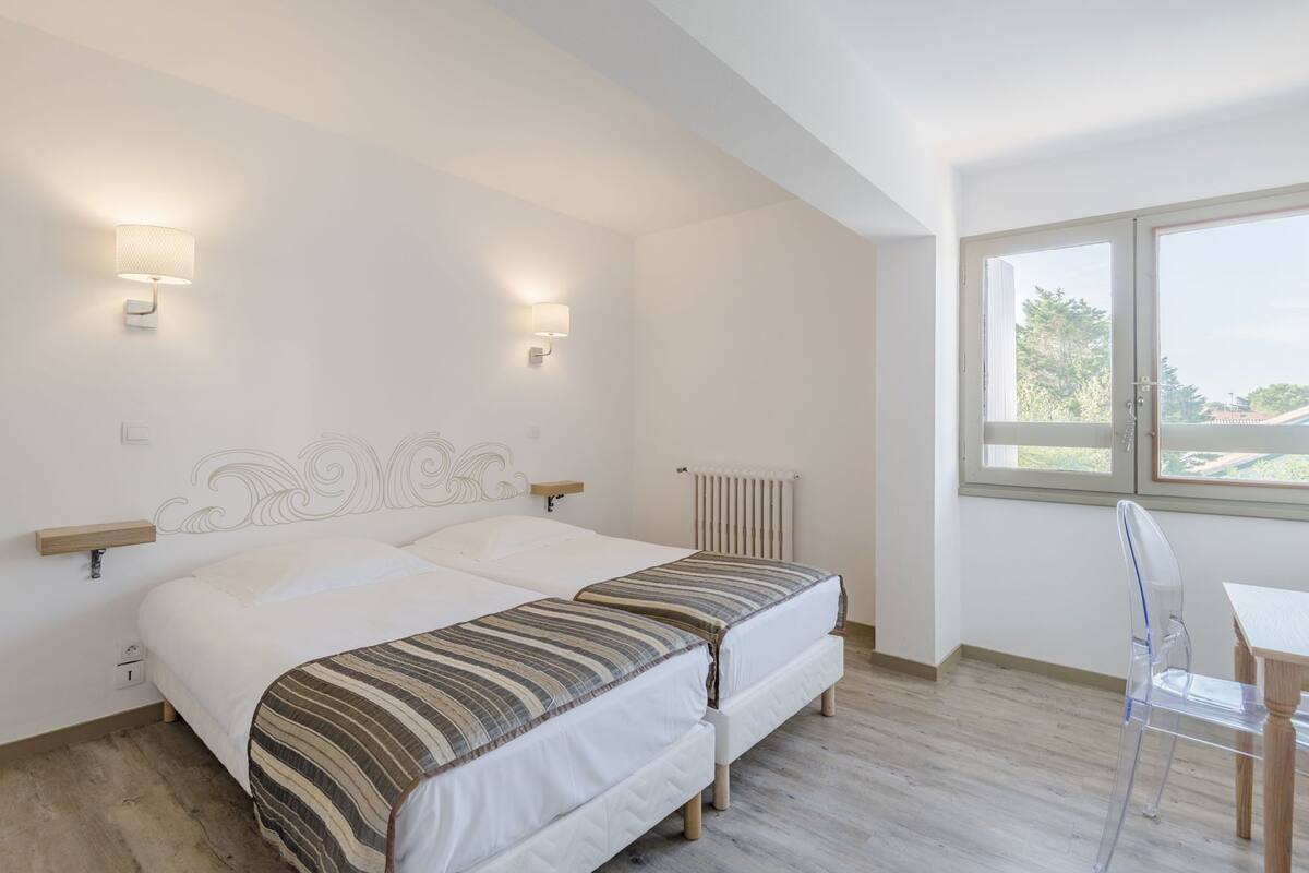 A bedroom with two beds, a radiator, a desk, and a chair.