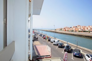 A coastal street with parked cars, a clear sky, and buildings in the background.
