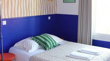 A room with a striped wall, a bed with a floral bedspread, a red pendant light, and a window with curtains.